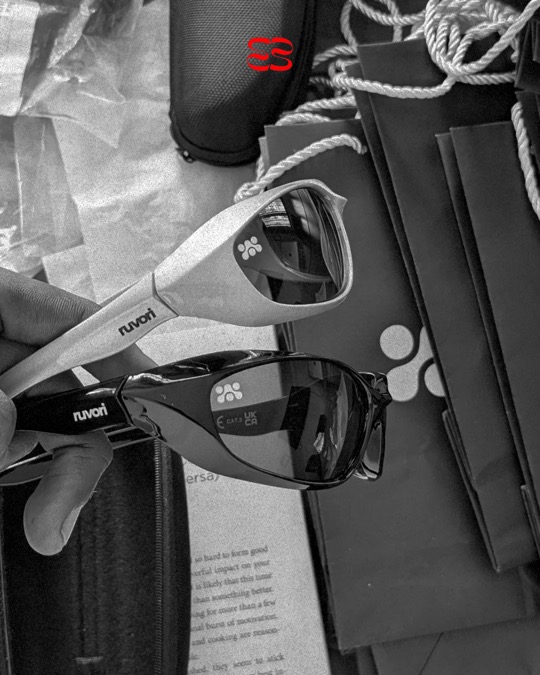 A hand holding the silver and black ruvori sunglasses above the ruvori bags and cases.