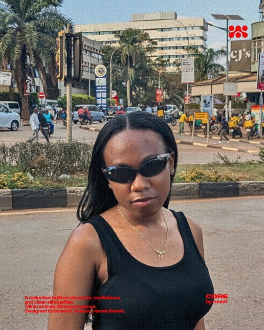 Woman in black Ruvori sunglasses and a black tank top on a busy city street, with palm trees, buildings and motorbike taxis behind her.